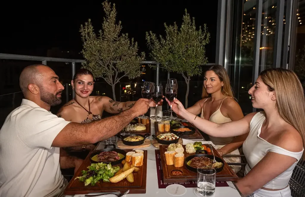 Friends toasting red wine during dinner at Memories L’Entrecôte’s Restaurant Rooftop in Larnaca